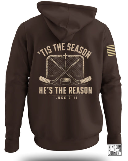 Brown hooded sweatshirt viewed from the back, featuring a distressed hockey graphic and the text "Tis The Season He's The Reason Luke 2:11."