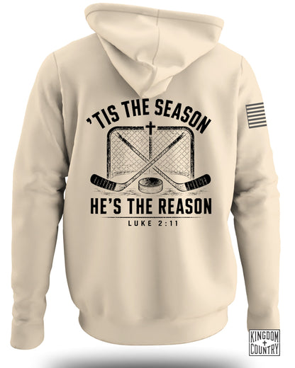 Back view of a beige hooded sweatshirt featuring hockey sticks, a net, and text reading Tis the Season He's the Reason Luke 2:11.