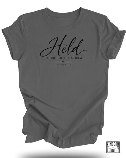 Dark gray t-shirt with "Held Through The Storm" and "Isaiah 41:10" text.