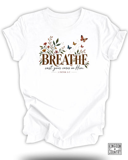 White t-shirt with "BREATHE cast your cares on Him 1 PETER 5:7" text and floral design.