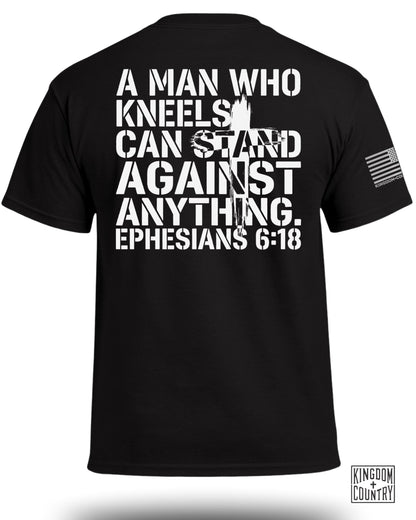 Black t-shirt with white text "A MAN WHO KNEELS CAN STAND AGAINST ANYTHING. EPHESIANS 6:18."