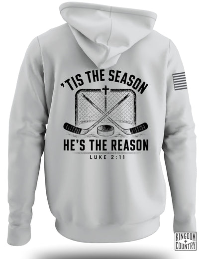Back view of a white hooded sweatshirt featuring a black graphic of crossed hockey sticks, a net, a puck, and the text "'Tis the Season, He's the Reason, Luke 2:11."