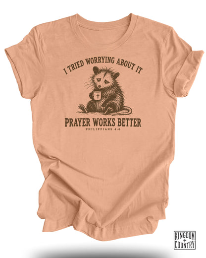 Peach t-shirt with a possum holding a coffee cup, text: "I tried worrying about it. Prayer works better. Philippians 4:6"