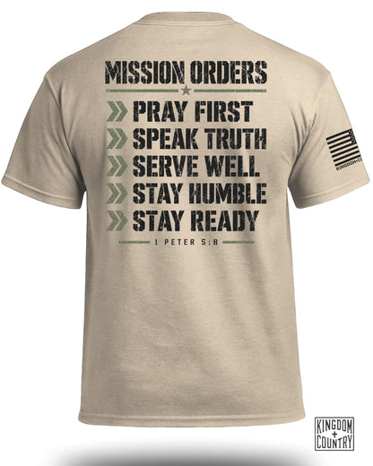 Tan t-shirt with black distressed text: "MISSION ORDERS PRAY FIRST SPEAK TRUTH SERVE WELL STAY HUMBLE STAY READY 1 PETER 5:8".