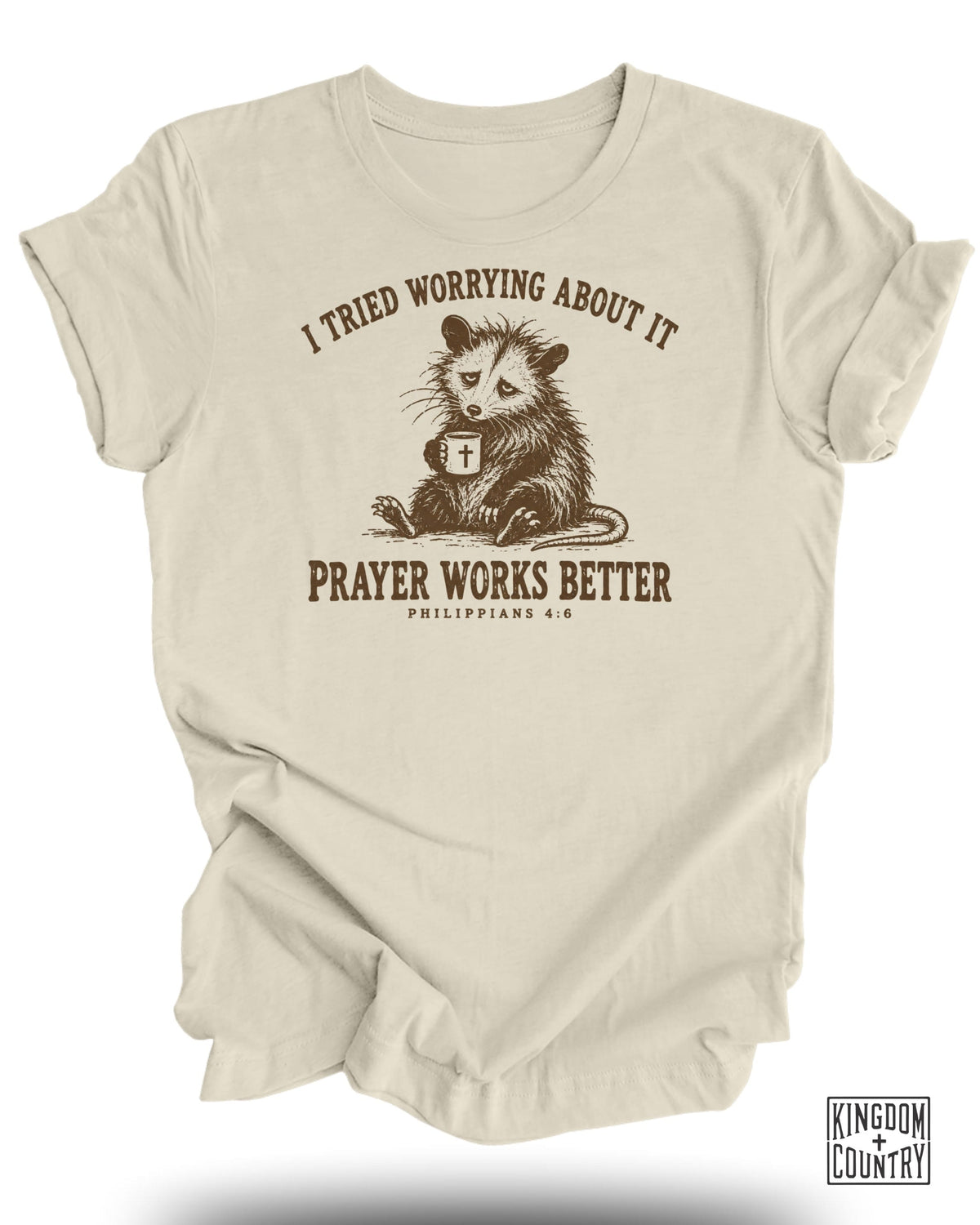 T-shirt with opossum holding a mug, text reads "I tried worrying about it. Prayer Works Better. Philippians 4:6"