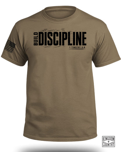Tan t-shirt with "BUILD DISCIPLINE 1 TIMOTHY 4:8" text and American flag patch.