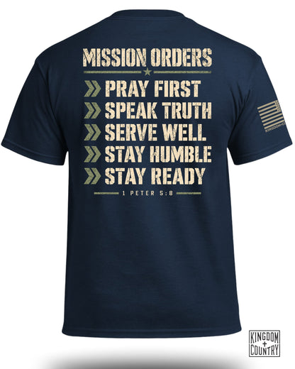 Navy t-shirt with "Mission Orders" and "1 Peter 5:8" text, and an American flag patch.
