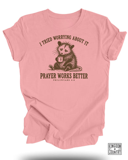 Pink t-shirt with opossum holding coffee mug and text: "I tried worrying about it. Prayer works better. Philippians 4:6."