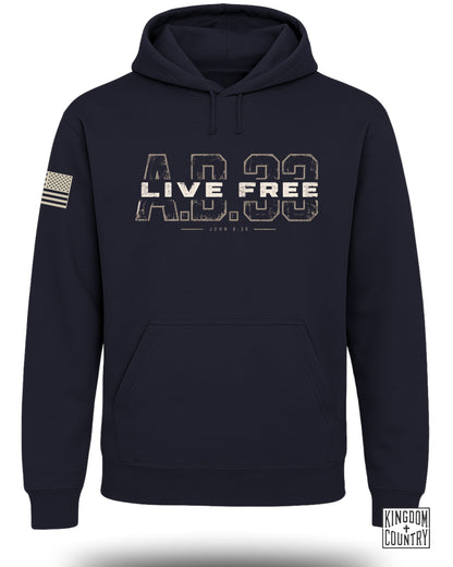 Dark navy blue pullover hoodie featuring a distressed white and tan chest graphic that reads AD 33 LIVE FREE with John 8:36 below, and an American flag patch on the left sleeve.