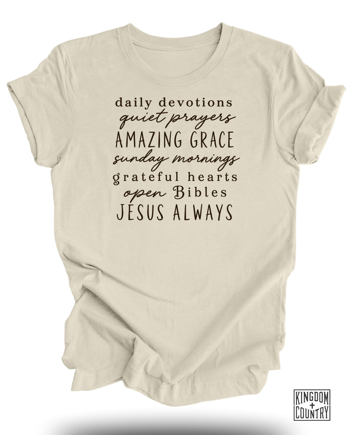 Light beige t-shirt with black text: "daily devotions quiet prayers AMAZING GRACE sunday mornings grateful hearts open Bibles JESUS ALWAYS"