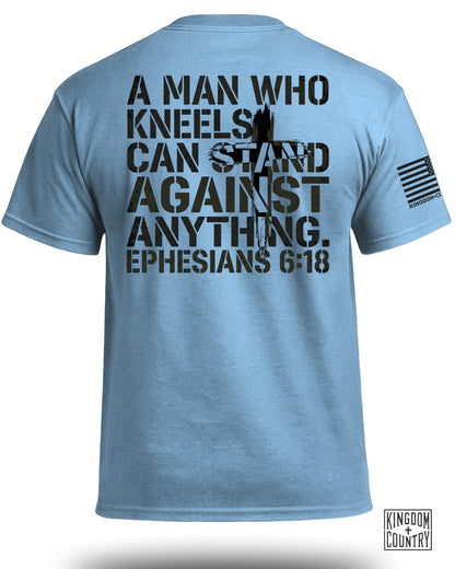 Light blue t-shirt with black text: "A MAN WHO KNEELS CAN STAND AGAINST ANYTHING. EPHESIANS 6:18"