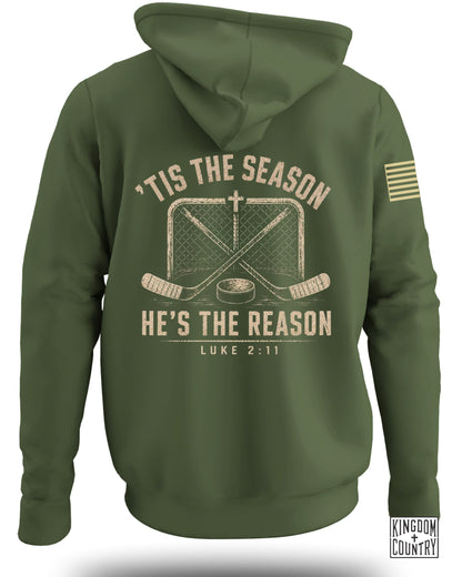 Olive green hooded sweatshirt viewed from the back, featuring a distressed hockey graphic and text reading 'Tis The Season He's The Reason Luke 2:11.