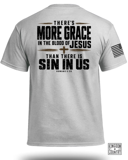 A light gray t-shirt displays text on the back that reads, THERE'S MORE GRACE IN THE BLOOD OF JESUS THAN THERE IS SIN IN US ROMANS 5:20 with a small cross symbol.