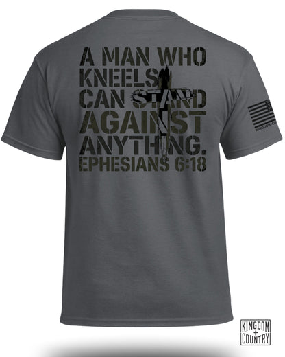 Dark grey t-shirt with "A man who kneels can stand against anything. Ephesians 6:18" text.