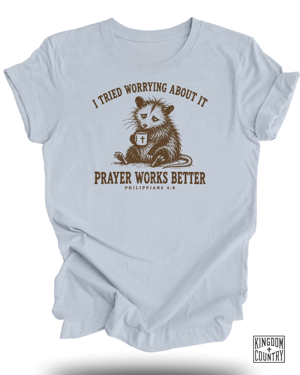 Light blue t-shirt with an opossum holding a mug, text "I tried worrying about it prayer works better".