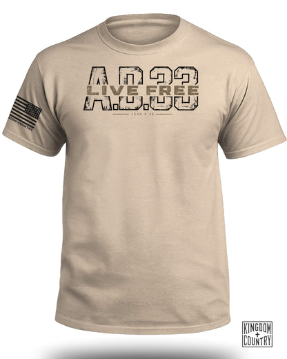 Desert tan crew neck t-shirt featuring the text "LIVE FREE A.D. 33" and a US flag on the sleeve.
