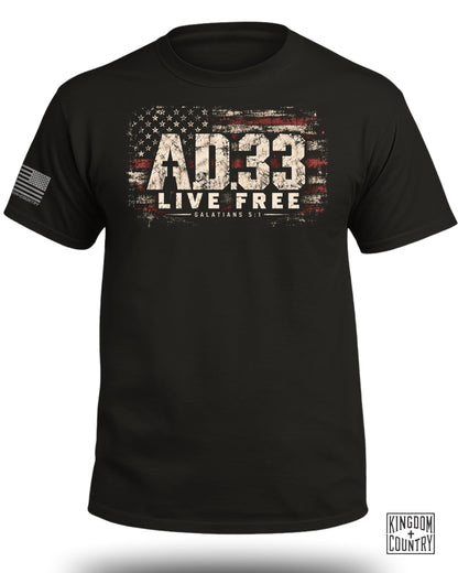 A black crewneck t-shirt featuring a distressed American flag graphic, text reading AD.33 LIVE FREE GALATIANS 5:1, and a sleeve flag.