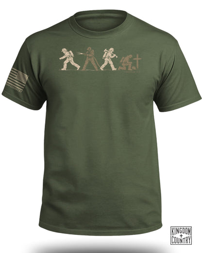 An olive green t-shirt featuring a graphic of four firefighters, a cross, and an American flag patch on the sleeve.